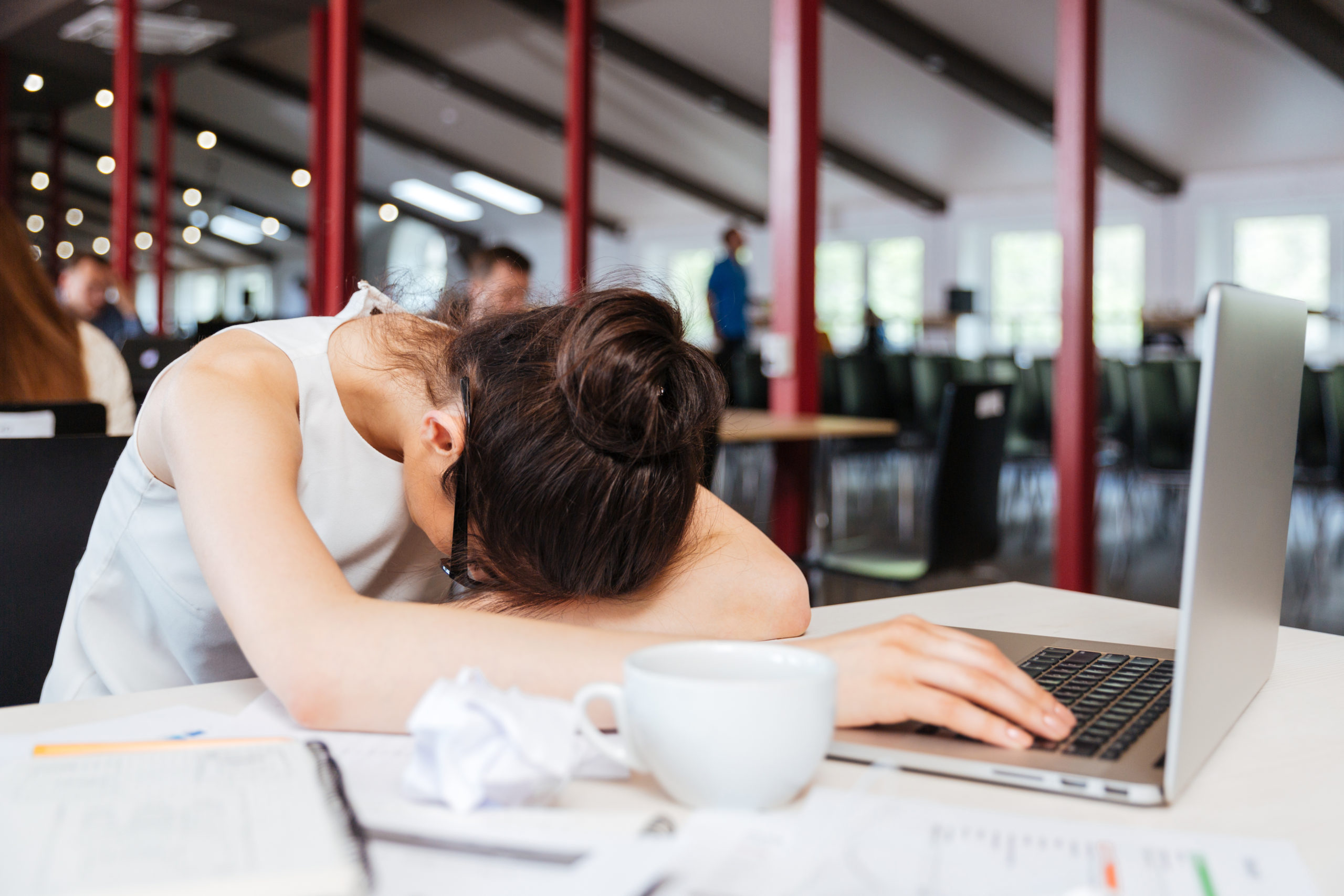 Exhausted fatigued young business woman sleeping on table with laptop at workplace